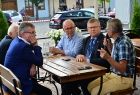 Marszałek Witold Kozłowski siedzi w towarzystwie trzech mężczyzn przy drewnianym stoliku. Jeden z nich trzyma mikrofon. Mężczyźni prowadzą ożywioną i wesołą rozmowę.