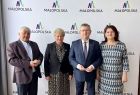 Marszałek Witold Kozłowski i lokalni samorządowcy. Wszyscy stoją na tle białej ścianki z napisem Małopolska i kolorowym logiem w kształcie litery M. 