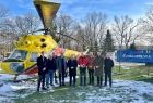 Uczestnicy wydarzenia wraz z Marszałkiem Witoldem Kozłowskim stoją przed żółtym śmigłowcem ratowniczym Mi-2 w Muzeum Ratownictwa.