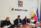 Wicemarszałek Łukasz Smółka i wicemarszałek Józef Gawron siedzą z dwiema kobietami przy stole w sali konferencyjnej. Na ścianie widoczny napis Małopolska i herb Małopolski, a obok stoją flagi.