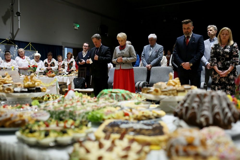 Goście zgromadzeni w sali na wydarzeniu stoją w rzędach, na stołach znajdują się potrawy wielkanocne