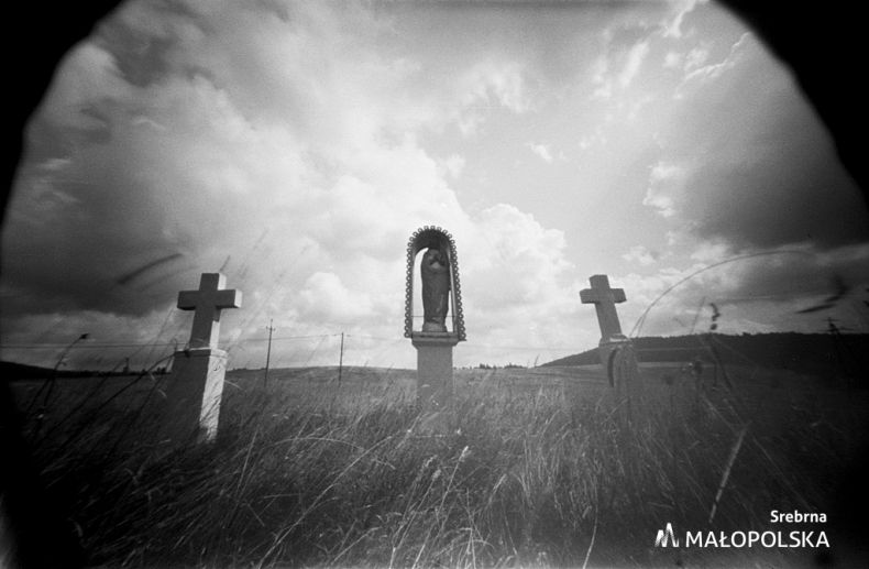 Zdjęcie czarno-białe w technice otworkowej, przedstawia 2 krzyże przydrożne a między nimi stoi kapliczka autorstwa Kamila Gubały