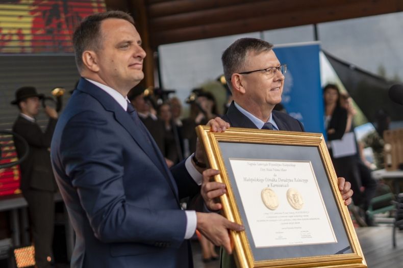 Marszałek Witold Kozłowski wręcza Złotą Polonie Minor dyrektorowi Małopolskiego Ośrodka Doradztwa Rolniczego w Karnowicach Dominikowi Paskowi . Mężczyźni stoją na scenie, trzymając wspólnie nagrodę oprawiona w pozłacana ramę. 