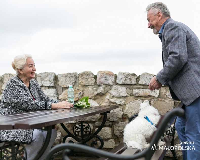 Seniorzy przy stoliku. Z tyłu widoczny zabytkowy mur.