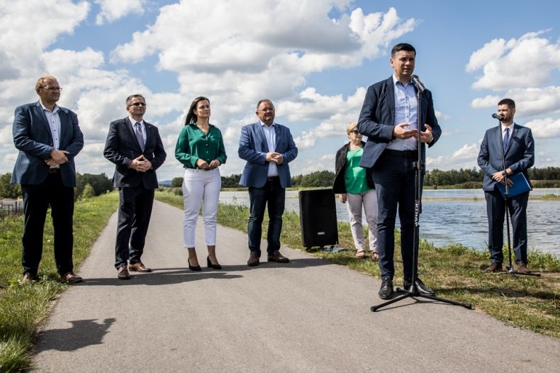 Wicemarszałek Łukasz Smółka przemawia podczas wydarzenia. Z tyłu widoczni ludzie stojący na drodze rowerowej.