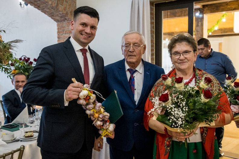 Wicemarszałek Łukasz Smółka trzyma pęczek czosnku. Obok stoją seniorzy.