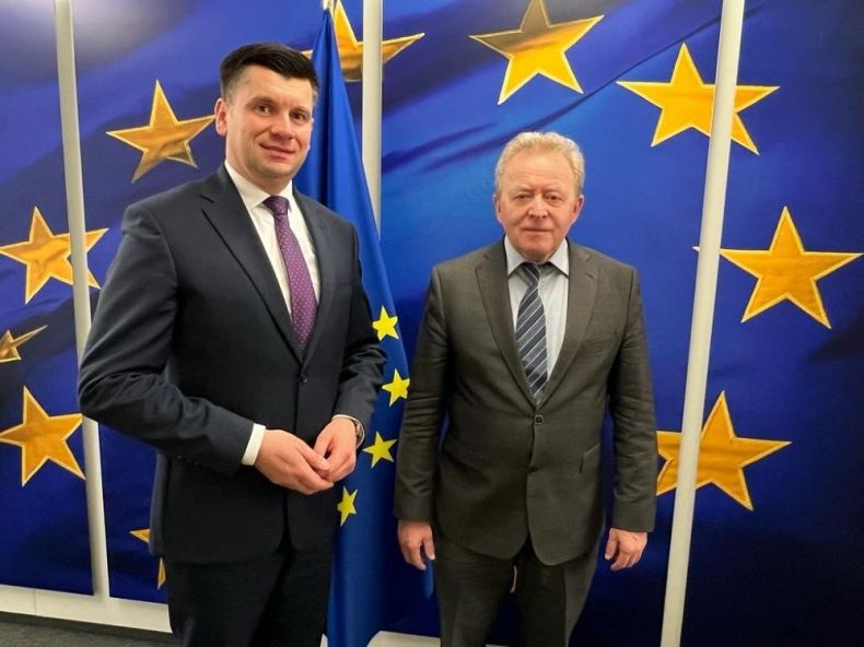 Wicemarszałek Łukasz Smółka stoi z komisarzem Januszem Wojciechowskim na tle flagi Unii Europejskiej.