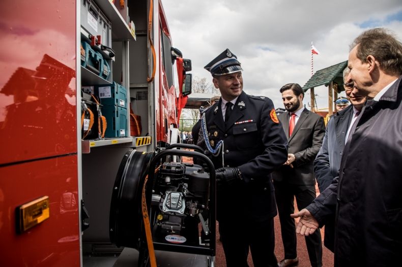 Wicemarszałek Łukasz Smółka ubrany w mundur ogląda sprzęt ratowniczy w samochodzie strażackim. Obok stoją pozostali uczestnicy wydarzenia.