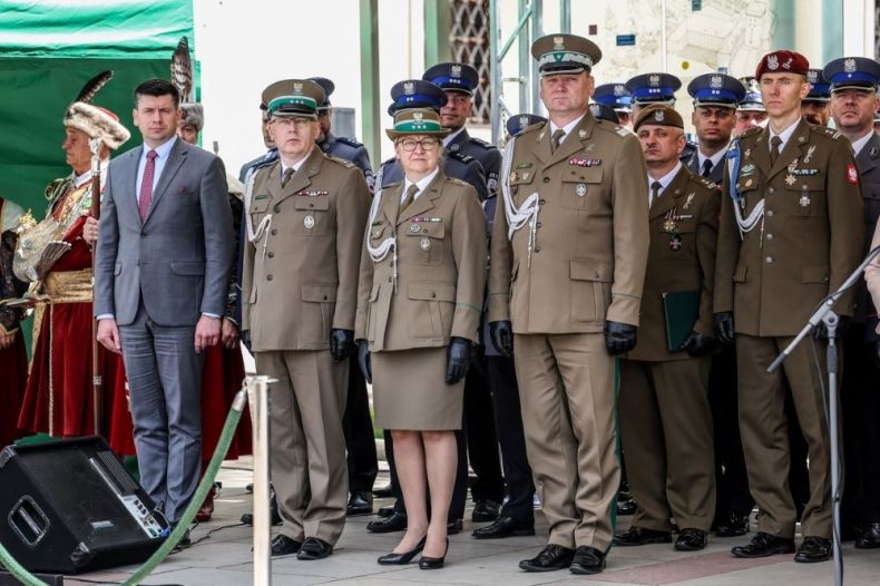 Wicemarszałek Łukasz Smółka stoi na trybunie z funkcjonariuszami straży granicznej.