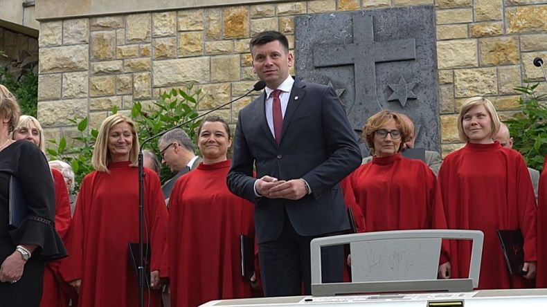 Wicemarszałek Łukasz Smółka stoi na tle chórzystów.