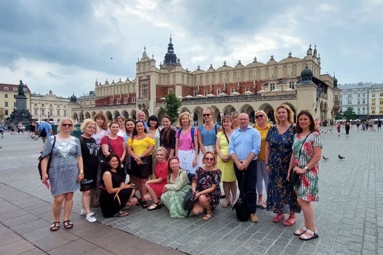 Grupa nauczycieli pozuje do wspólnego zdjęcia na tle Sukiennic w pogodny dzień