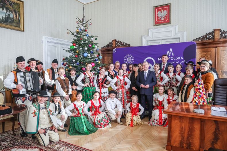 Grupa młodzieży i dzieci wraz z opiekunami, pozuję wspólnie do zdjęcia z Marszałkiem Witoldem Kozłowskim. Dzieci maja na sobie tradycyjne stroje ludowe. 