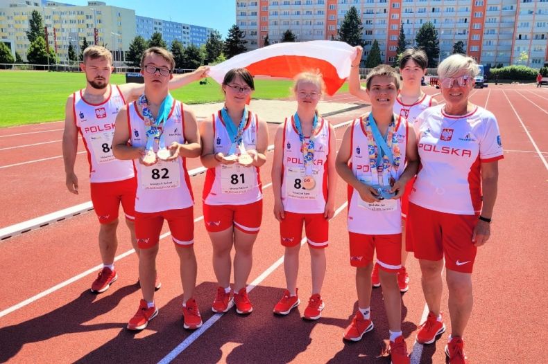 Grupa młodzieży w strojach sportowych stoi na bieżni trzymając biało-czerwoną flagę
