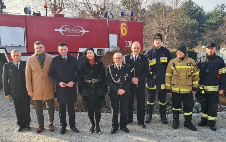 Wicemarszałek Łukasz Smółka i Iwona Gibas z zarządu województwa stoją z innymi uczestnikami wydarzenia i strażakami. Z tyłu widoczny wóz strażacki.