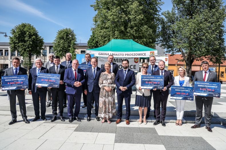 Beneficjenci stoją na rynku w Proszowicach i trzymają czeki.