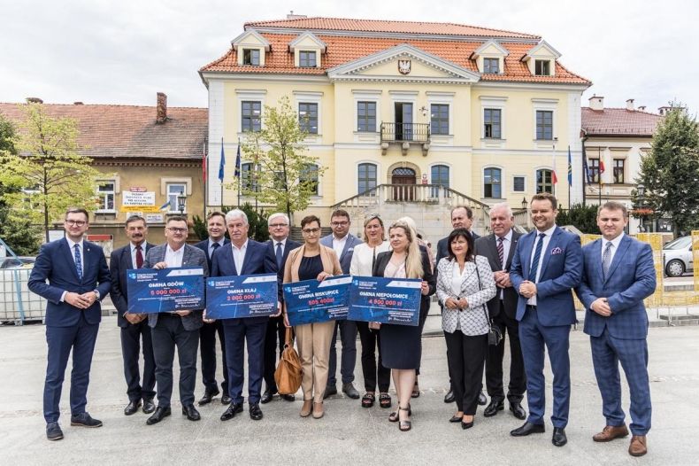 Grupa uczestników wydarzenia w Wieliczce trzyma symboliczne czeki na inwestycje