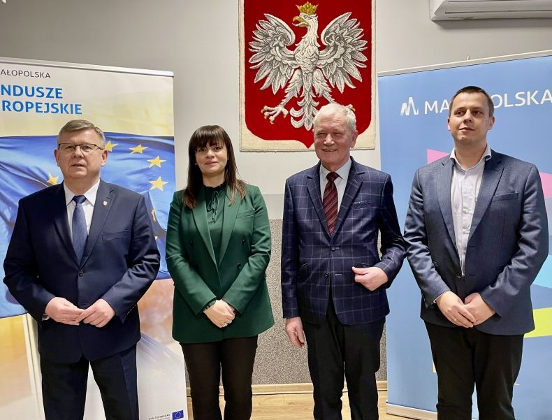Zdjęcie grupowe. Marszałek, wójt, dyrekcja i kierownictwo ZDW. W tle godło, logo Małopolska oraz fundusze europejskie. 
