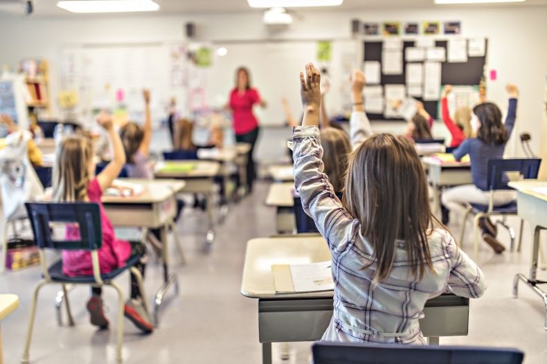 widok na klasę szkolną podczas lekcji - jedno z dzieci zgłasza się do odpowiedzi