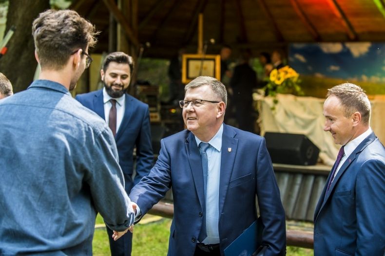 Marszałek Witold Kozłowski, podaję rękę mężczyźnie stojącemu tyłem do zdjęcia, po prawej stronie marszałka stoi wójt gminy Grybów. W tle widać scenę i stojącego i Sekretarza stanu w ministerstwie rolnictwa Norberta Kaczmarczyka.