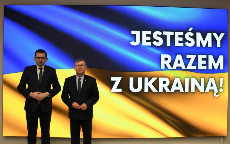 marszałek Małopolski i wojewoda na tle flagi Ukrainy. w tle napis "Jesteśmy razem z Ukrainą"