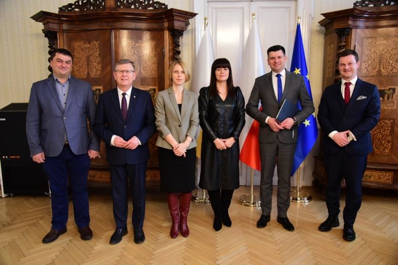 marszałek Witold Kozłowski, wicemarszałek Łukasz Smółka oraz kilka osób stoi na tle flag i pozuje do zdjęcia
