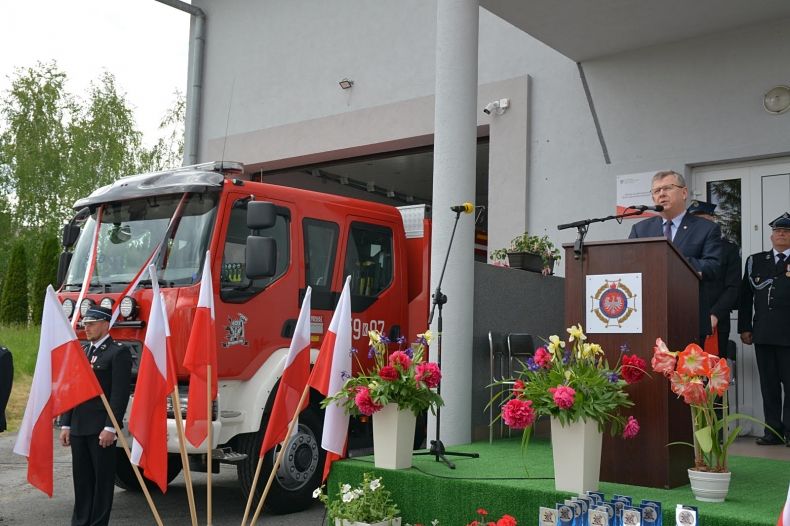 marszałek na scenie podczas wystąpienia, obok duży wóz strażacki