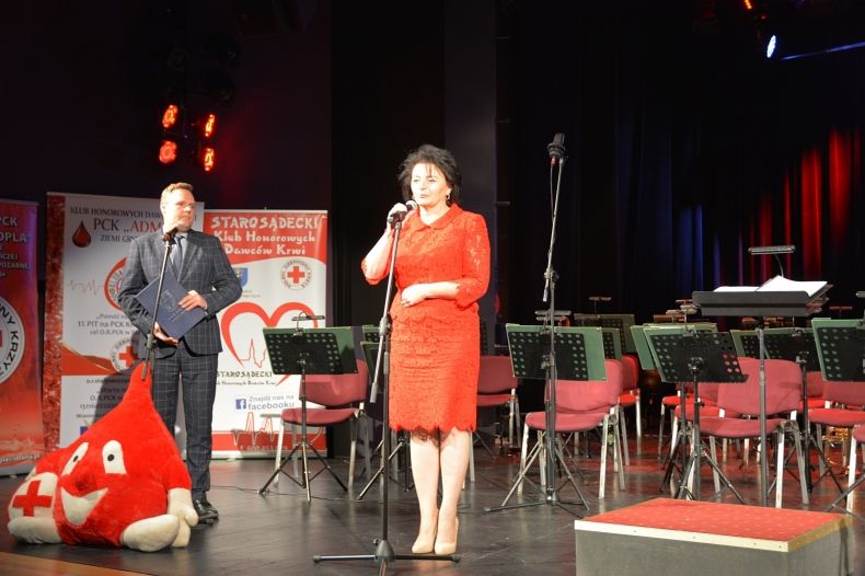 Radna województwa Małopolskiego Jadwiga Wójtowicz, stoi na scenie. W tle widać logo Polskiego Czerwonego Krzyża. 
