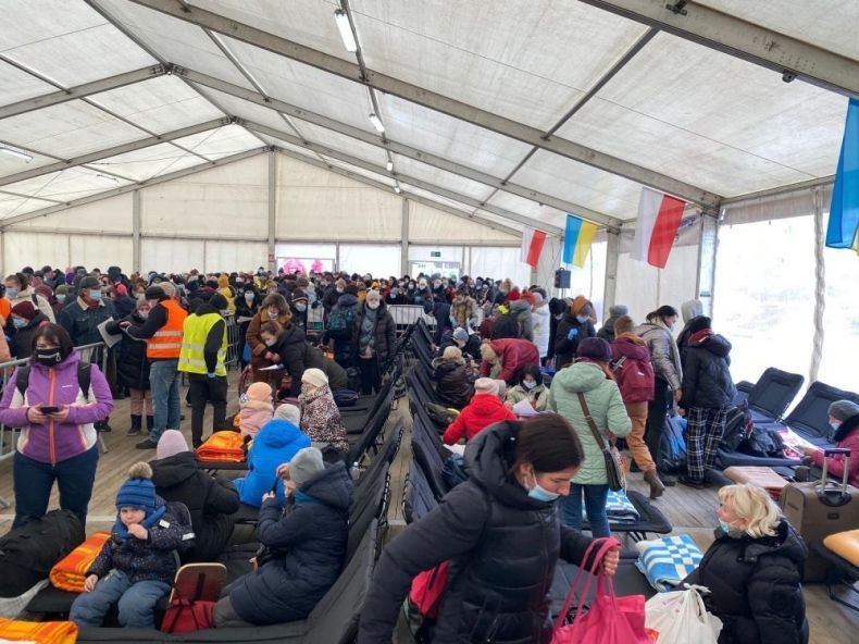 Wnętrze pawilonu dla uchodźców z Ukrainy. Widoczni ludzie i flagi Polski i Ukrainy przy ścianach.