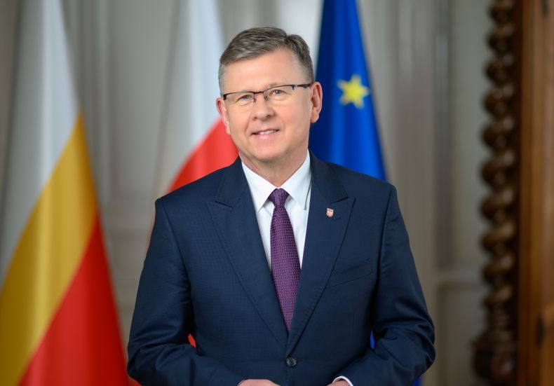 marszałek Kozłowski stoi na tle flag: wojewódzkiej, krajowej i UE