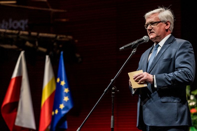 Wicemarszałek Józef Gawron stoi i mówi do mikrofonu. W tle widoczne flagi: Polski, Małopolski i Unii Europejskiej.