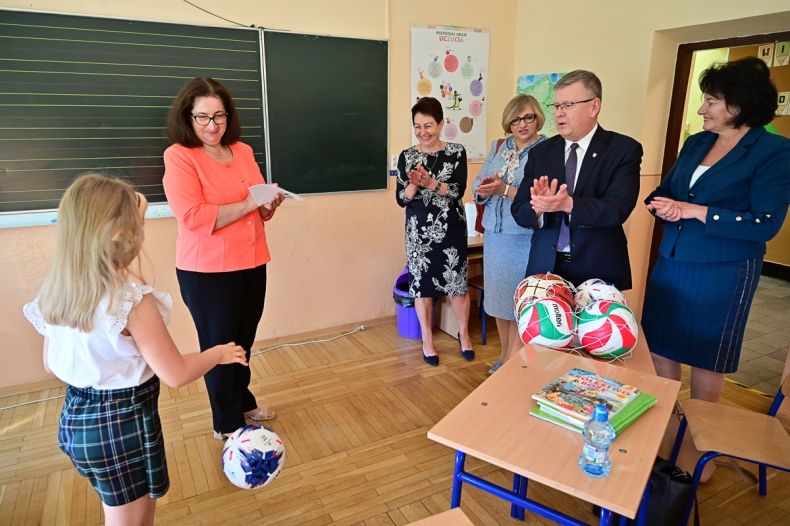 Wnętrze klasy, przy tablicy stoi nauczycielka, obok niej widać uczennice, z lewej strony stoją marszałek Witold Kozłowski i radna Jadwiga Wójtowicz. 