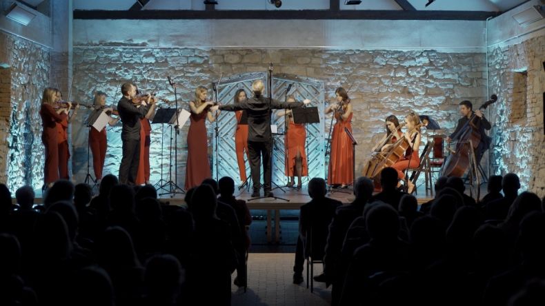 Grupa ludzi w galowych strojach trzyma w rękach instrumenty muzyczne