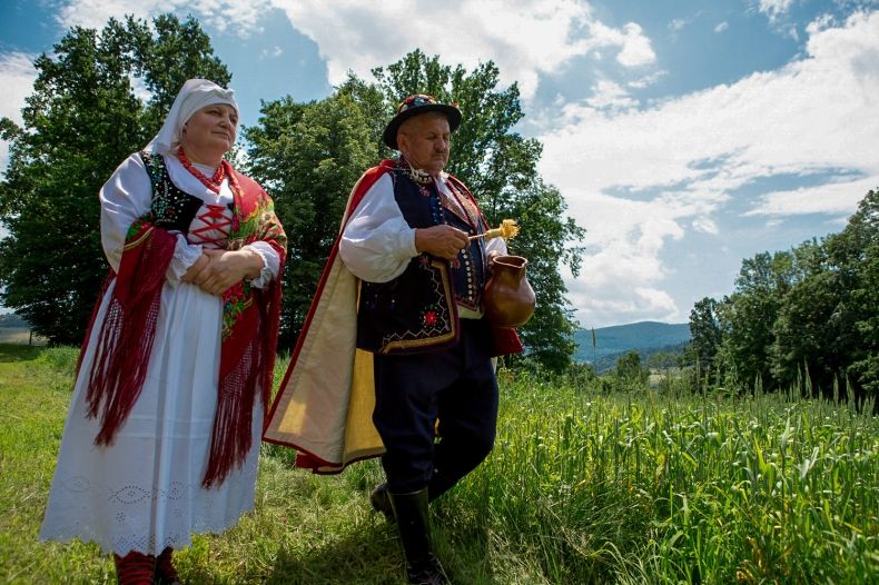 Mężczyzna i kobieta w strojach ludowych idą przez łąkę