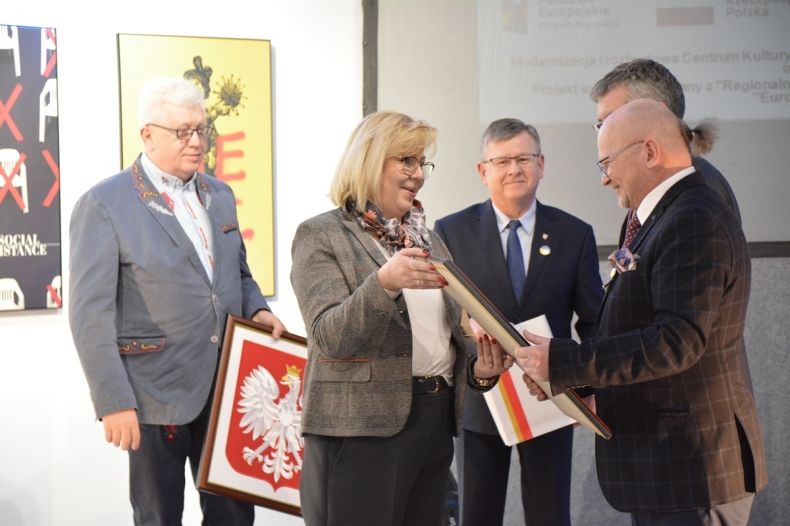 Na pierwszym planie widać radną województwa MArte Mordarską, radnego Stanisława Pasonia i Marszałka małopolski Witolda Kozłowskiego, przekazują oni godła Małopolski i Polski. 