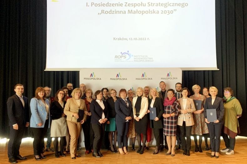 Uczestnicy spotkania pozują do wspólnego zdjęcia na tle ekranu z napisem "Pierwsze posiedzenie Zespołu Strategicznego Rodzinna Małopolska 2030"