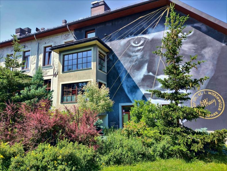 Budynek Teatru Witkacego od strony Sceny Witkacego w słoneczny letni dzień. Na ścianie widać duży mural przedstawiający autoportret Witkacego.