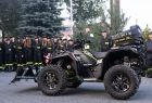 Strażacy stoją w rzędzie, przed nimi na placu stoi quad