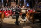 Wicemarszałek Łukasz Smółka przekazuje opatowi medal Polonia Minor. Z tyłu stoi zespół "Mazowsze".