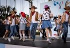 Dzieci w kowbojskich strojach tańczą na scenie trzymając się pod ręce