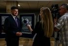 Wicemarszałek Łukasz Smółka stoi przed dziennikarką z telewizji i przed kamerą.