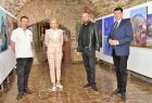 Wicemarszałek Łukasz Smółka stoi wewnątrz galerii z obrazami w towarzystwie ludzi.