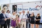 Wicemarszałek Łukasz Smółka stoi z prezydentem Andrzejem Dudą i innymi uczestnikami wydarzenia przed mammobusem.