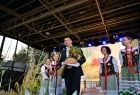Wicemarszałek Łukasz Smółka stoi na scenie i trzyma chleb. Obok stoją kobiety.