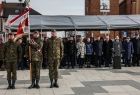 Żołnierze trzymają sztandar, w tle namiot pod którym stoją zaproszeni goście