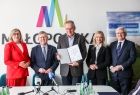 Mężczyzna w garniturze prezentuje podpisaną umowę. Obok marszałkowie i panie poseł.
