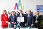 Mężczyzna w garniturze z poszetką prezentuje umowę. Obok marszałkowie i panie poseł.