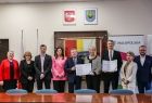 Wspólne zdjęcie uczestników wydarzenia w Brzeszczach. W centrum kadru: marszałek Witold Kozłowski, Iwona Gibas z zarządu województwa oraz burmistrz Radosław Szot prezentują podpisaną umowę 