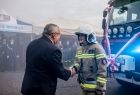 Minister Andrzej Adamczyk podaje rękę strażakowi. Za nim stoi wóz strażacki.