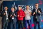 zdjęcie grupowe: marszałek, burmistrz i zawodnicy kickboxingu, na granatowej ściance z logotypem igrzysk