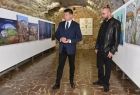 Wicemarszałek Łukasz Smółka stoi wewnątrz galerii z obrazami w towarzystwie mężczyzny.